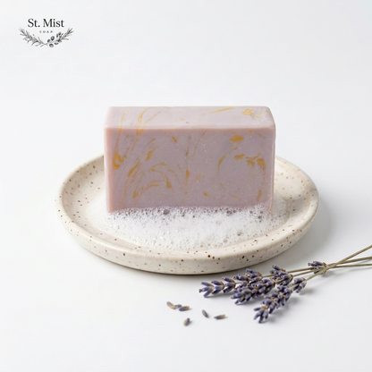 St. Mist Soap lavender bar with purple and gold swirls on a speckled ceramic dish with fresh lavender sprigs.