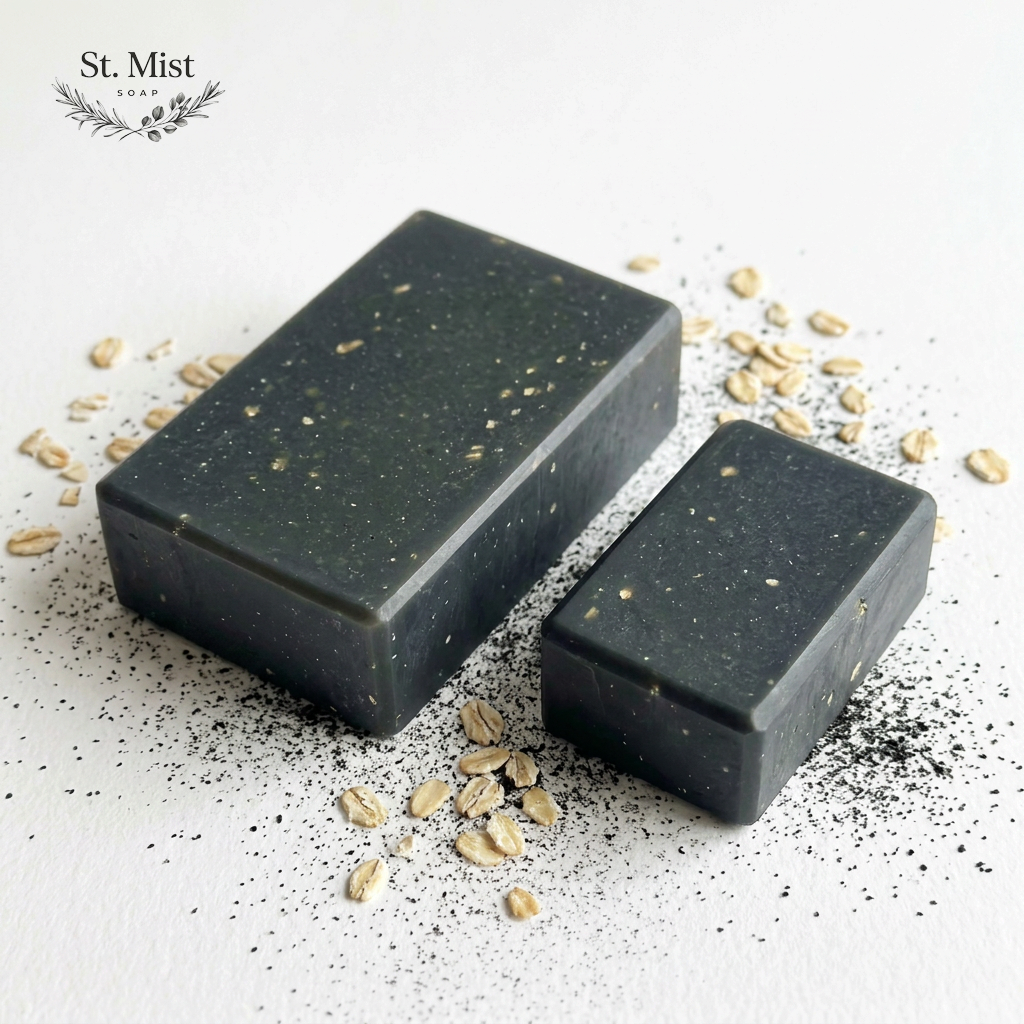 St. Mist Soap handcrafted black charcoal and oatmeal soap bars on a white background with scattered oat flakes.